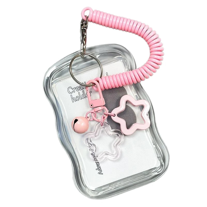 A clear plastic card holder with a pink silicone strap and a heart-shaped charm attached to a metal keychain.