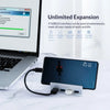 A black multi-port USB 3.0 hub with a clip is shown next to a laptop and a smartphone.
