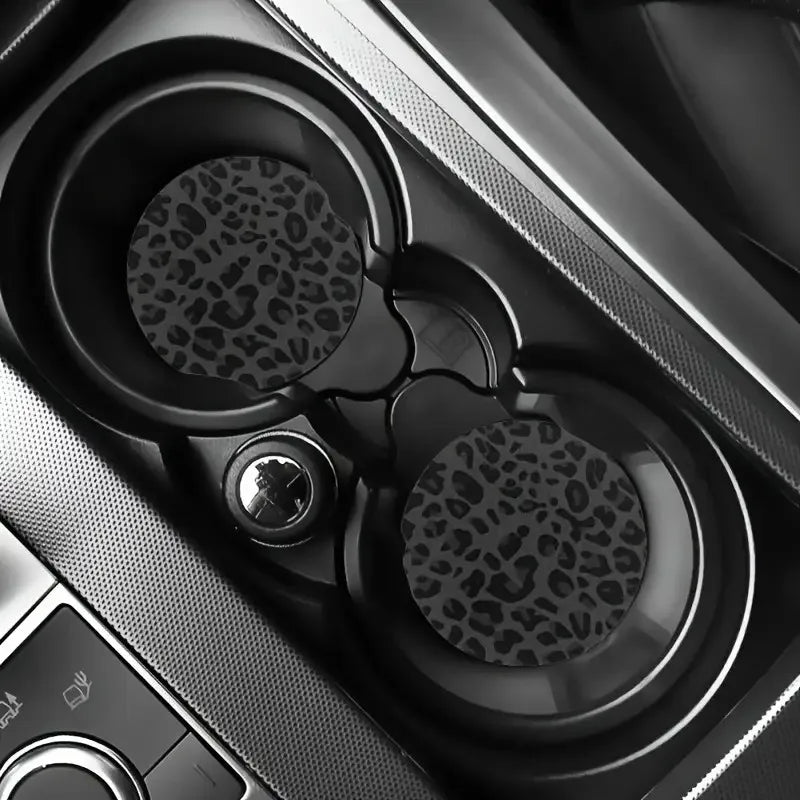 Close-up view of two leopard print non-slip leather car cup holder coasters in a dark interior setting.