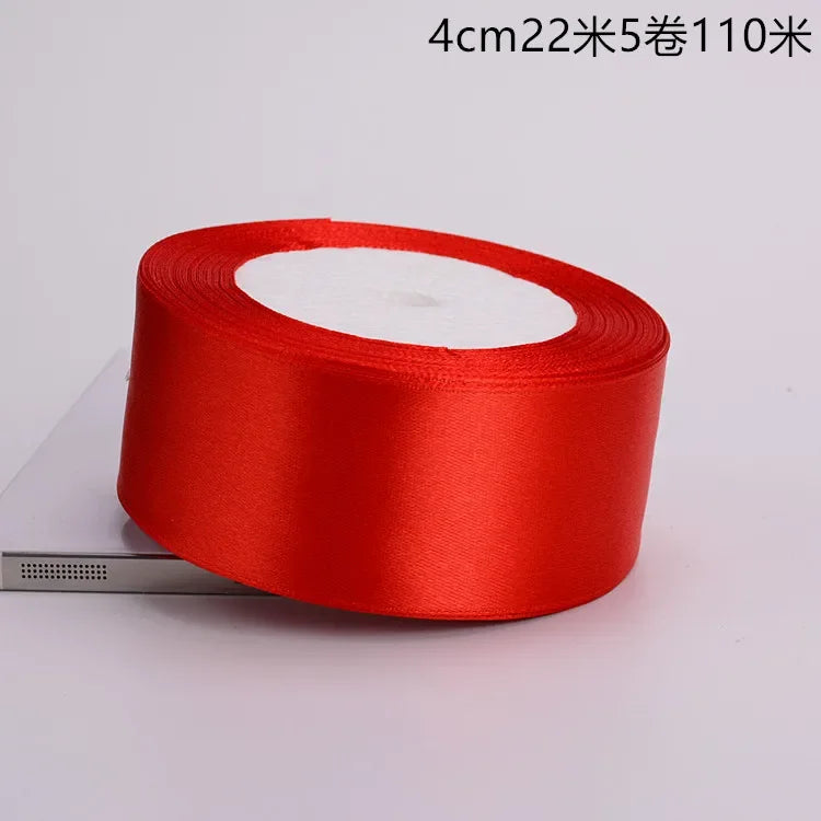 A roll of bright red satin ribbon is shown on a white background.