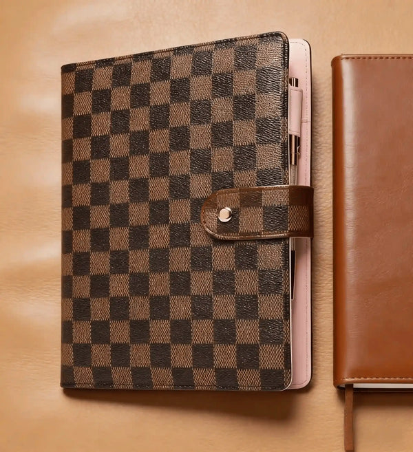 A black and brown checkered PU leather portfolio with a leather strap resting on a tan leather surface.