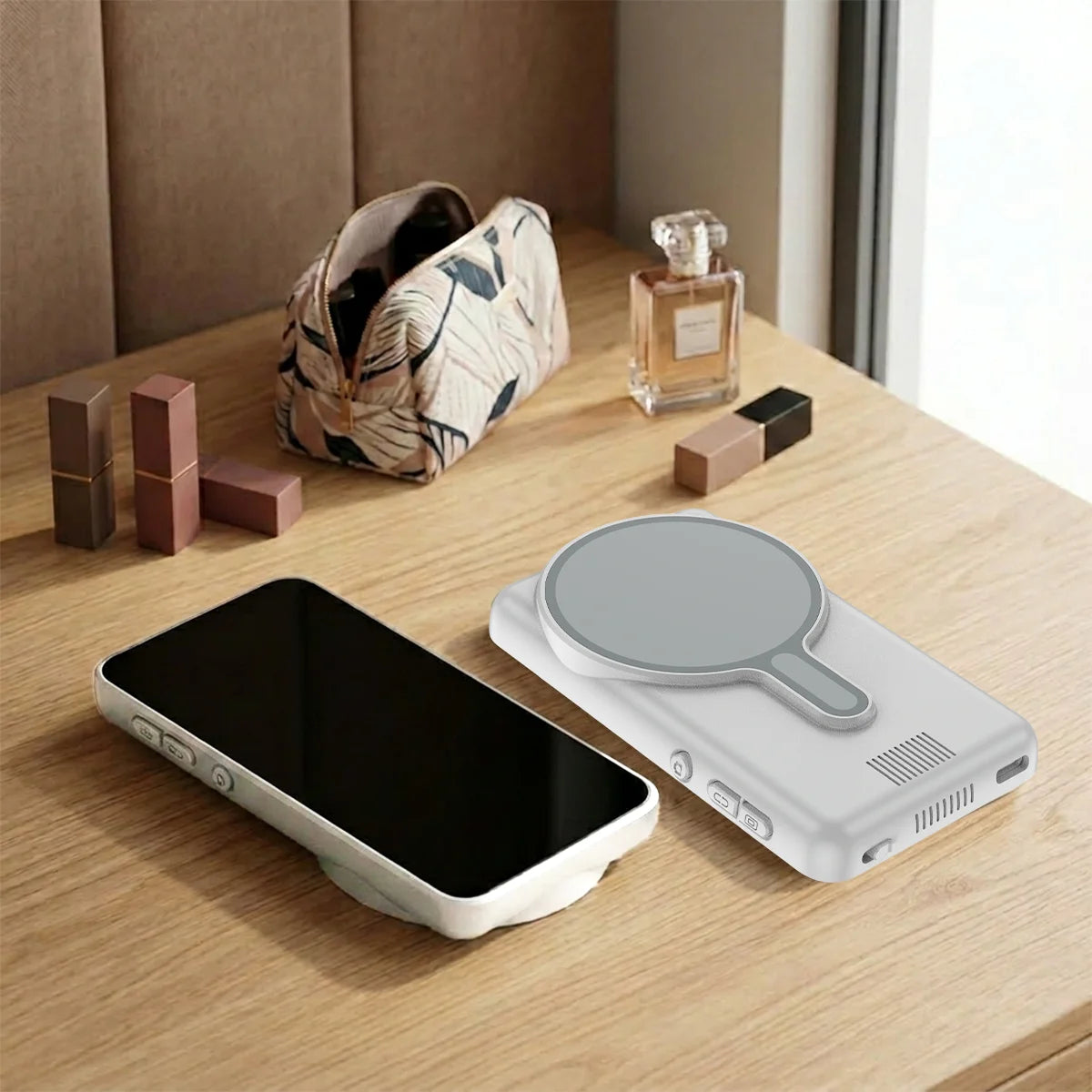 A smartphone is placed next to a magnetic monitor screen, with perfume bottles and a patterned fabric in the background.