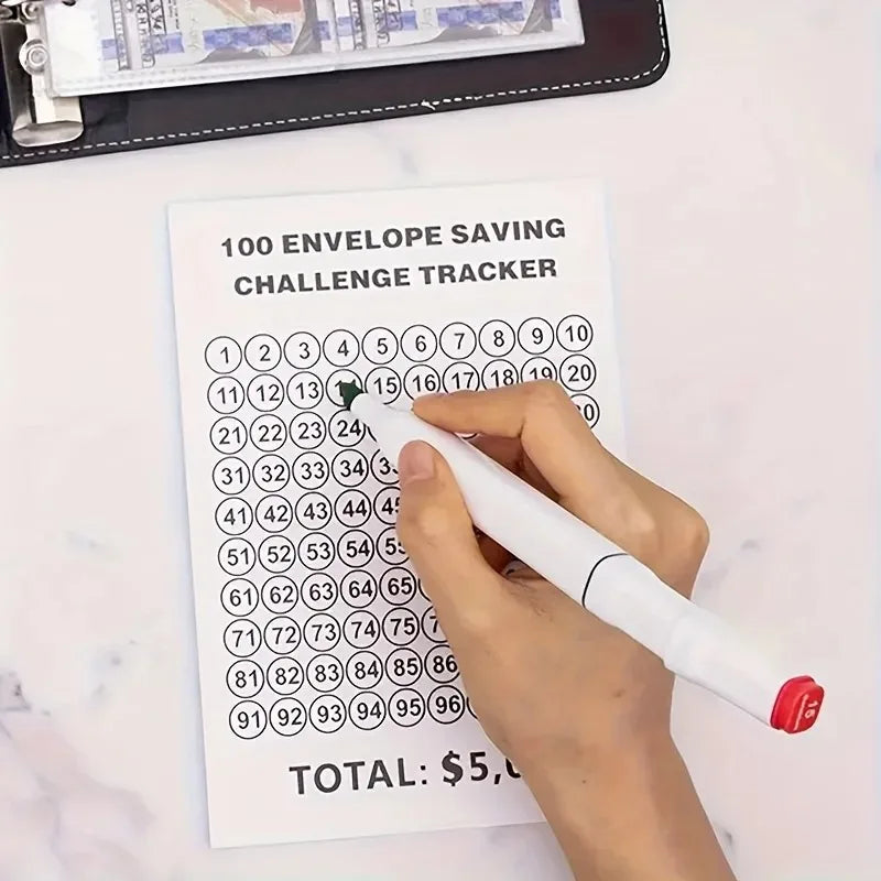 A hand is writing on a tracker sheet for a 100 envelope saving challenge, next to a stack of cash