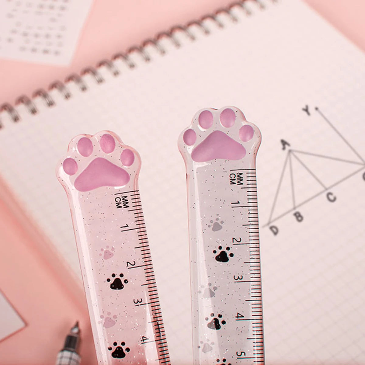 A pink plastic ruler shaped like a cat paw measures 15 cm and features paw prints along the markings.
