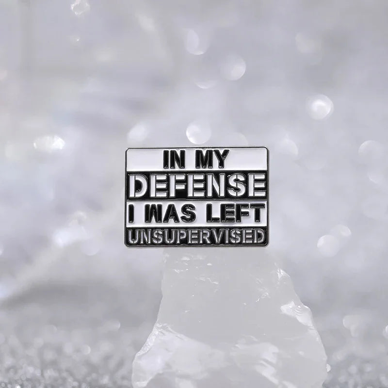 A silver enamel pin with the text In My Defense I Was Left Unsupervised on a white background.