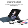 A desktop charger is shown with a cable charging an iPhone on a laptop surface.