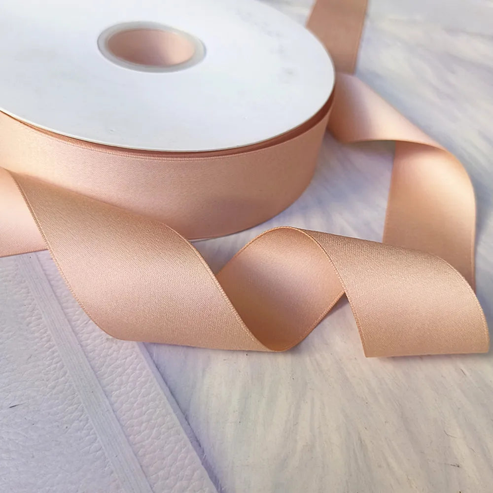 Roll of matte finish satin ribbon in a nude pink color with a visible core.