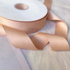 Roll of matte finish satin ribbon in a nude pink color with a visible core.