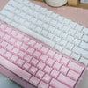 A close-up view of a pink mechanical keyboard with white keycaps and a translucent pink keycap set.