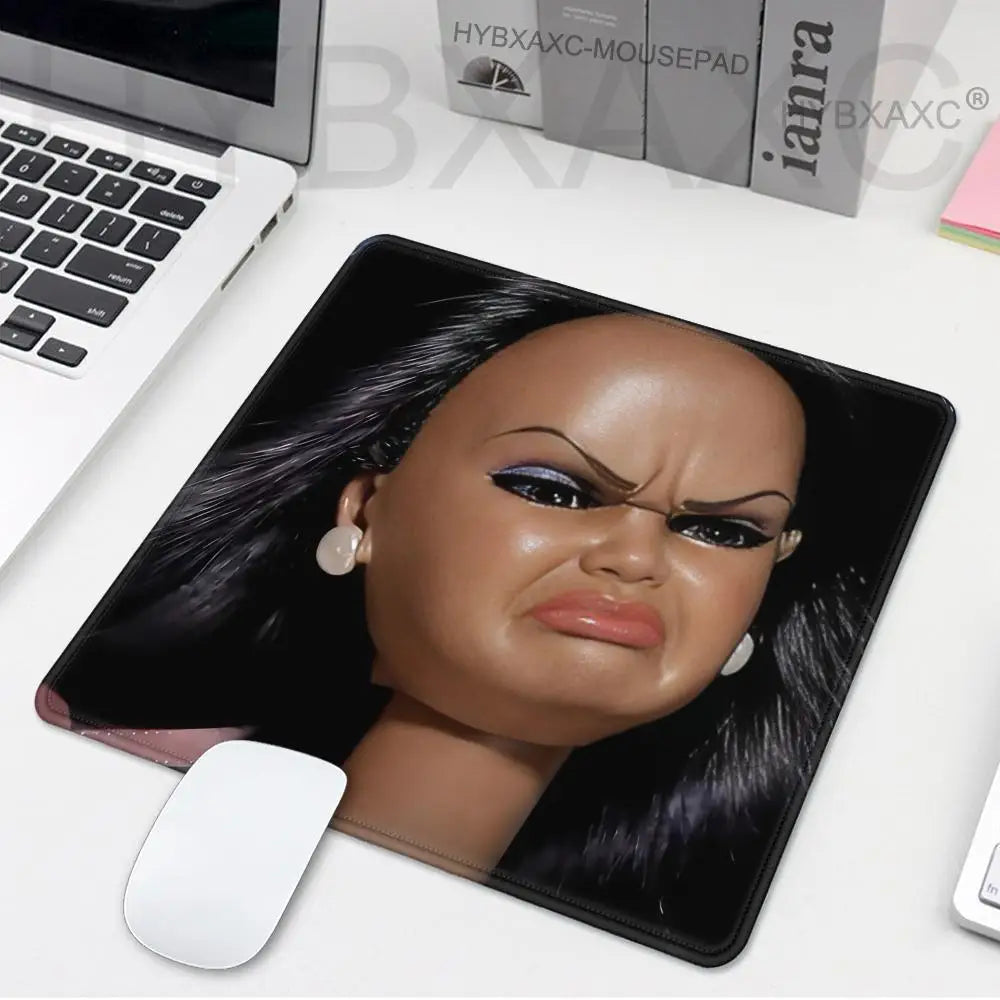 A realistic doll face print on a black mouse pad next to a laptop and a mouse.