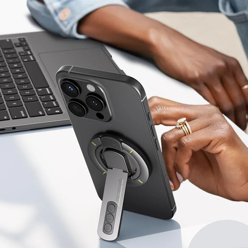 A hand holds a black smartphone with a magnetic ring holder attached, resting on a laptop.