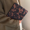 Dunkelbraunes Leopardenmuster-Leder-Tablet-Cover wird in der Hand einer Person gegen einen neutralen Mantel gehalten.