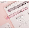 A pink plastic straight ruler marked with cat paw shapes is shown next to graph paper and a pencil.