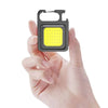 A hand holds a compact COB keychain flashlight with a magnetic base and rechargeable battery.