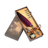 A wooden box containing a feather dip pen set with various nibs and a small ink bottle, resting on a map background.