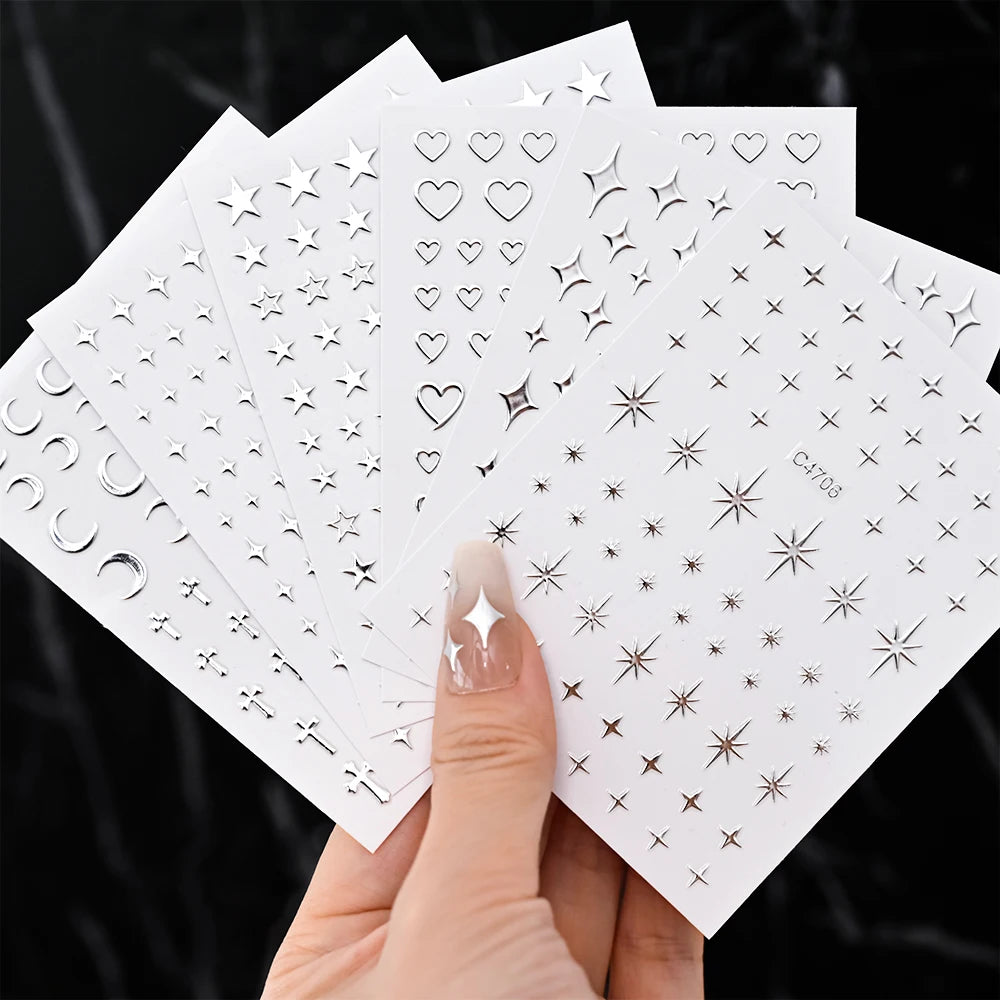 A hand holds a set of metallic 3D star nail art stickers on white cards.