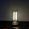 A clear glass Edison style light bulb with a filament and a touch dimming feature sits on a dark surface.