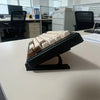 A black adjustable keyboard tray riser set with white and brown keys resting on a white desk.