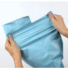 A hand is holding a light blue reusable waterproof poly shipping bag.
