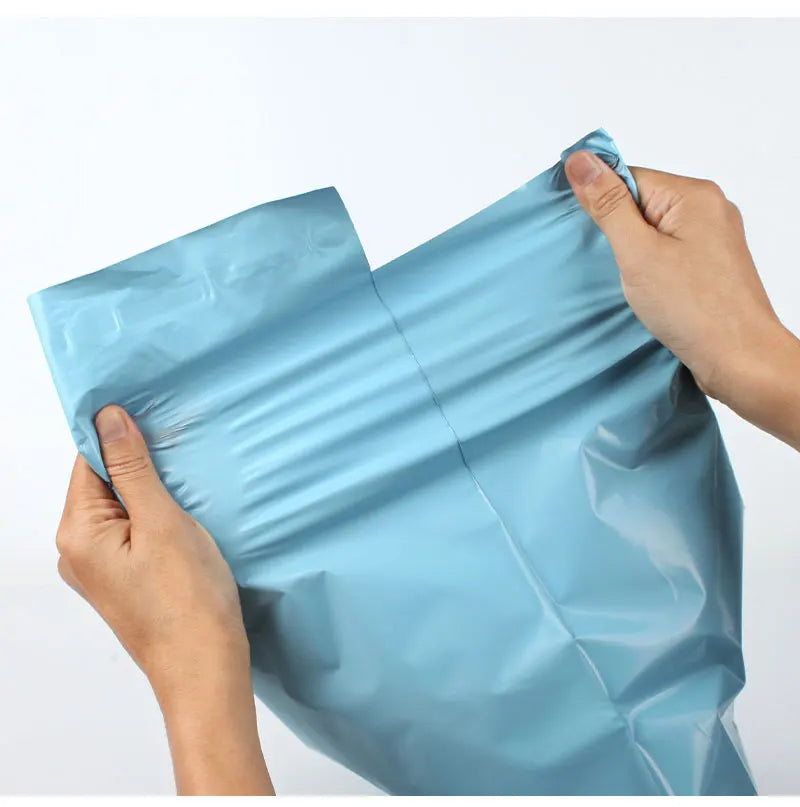 A hand is holding a light blue reusable waterproof poly shipping bag.