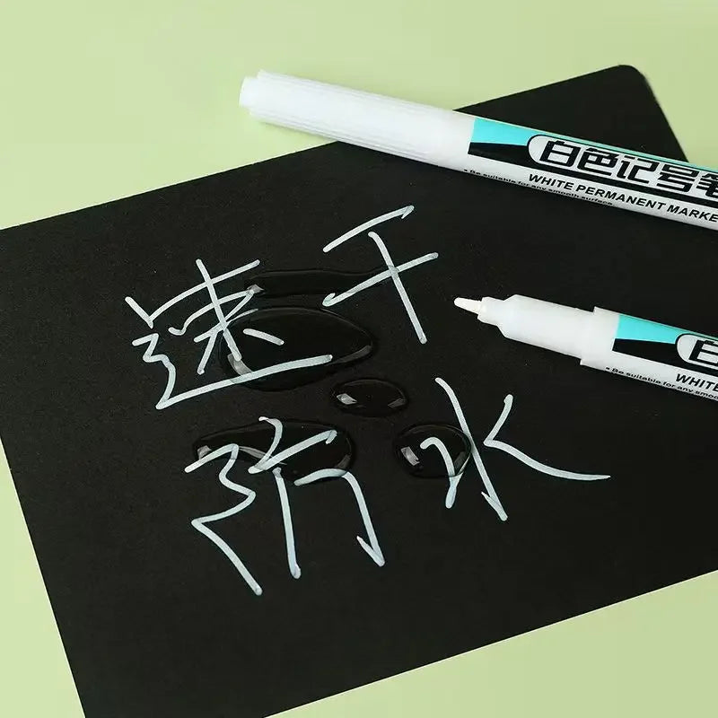 A white permanent marker pen is shown writing Chinese characters on a black surface.