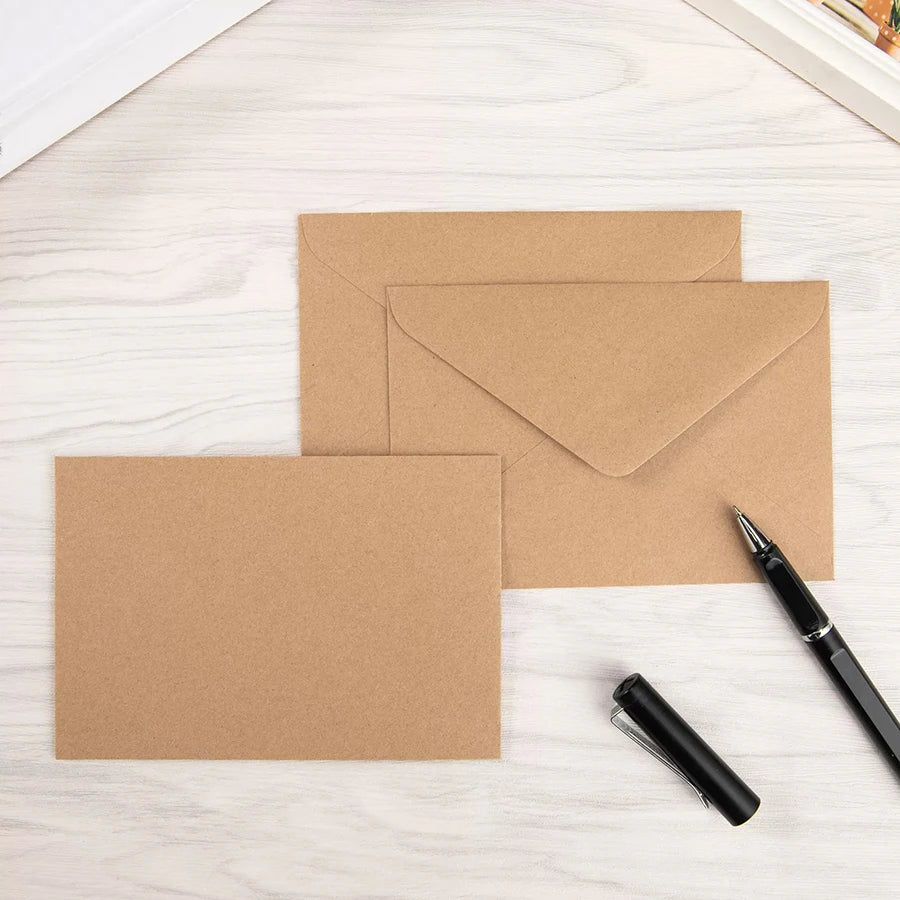 Ein Stapel brauner Kraft-Briefumschläge und ein schwarzer Stift auf einer hellen Holzoberfläche.