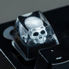 A clear resin skull mechanical keycap resting on a black surface.