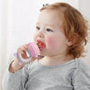 A baby is using a pink silicone fruit feeder set to feed a piece of fruit.