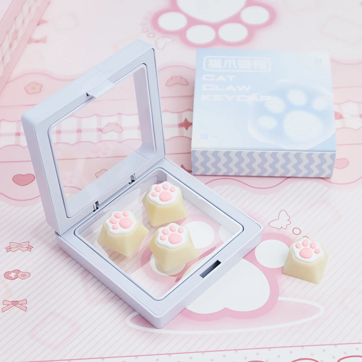 A white keycap puller is shown with pink cat paw and heart themed keycaps resting inside, next to the packaging box.