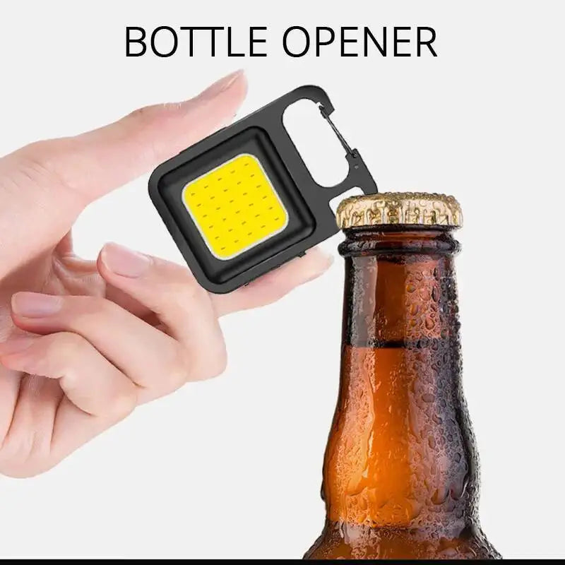 A hand holds a black bottle opener tool next to an amber glass bottle.