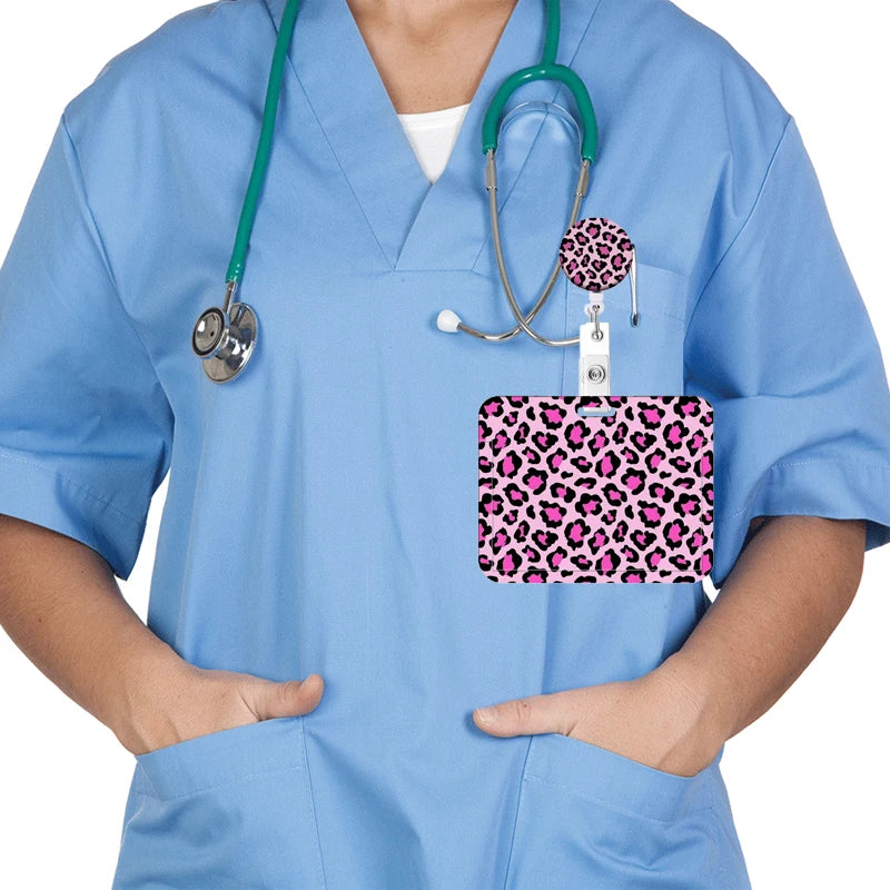 A person wearing light blue scrubs holds a leopard print retractable badge holder with a stethoscope attached.