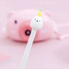 A white gel pen with a cute cartoon fruit topper is positioned in front of a pink piggy bank.