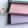 A stack of tearable lined writing pads in pink, purple, and dark gray.
