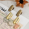 A set of brass metal beetle binder clips resting on a piece of aged paper and dried flower petals.