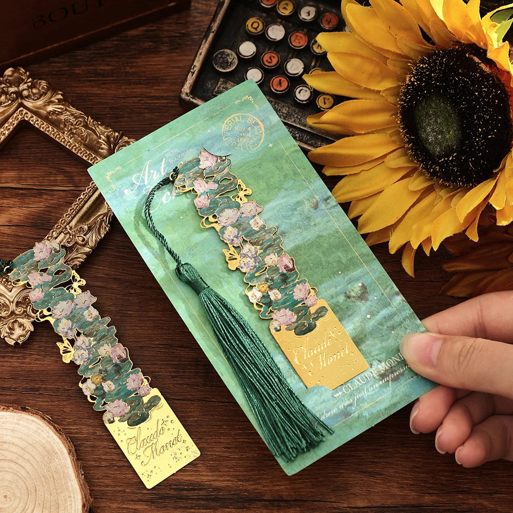 A vintage artistic metal bookmark with a green tassel resting on a green card against a dark wooden background.