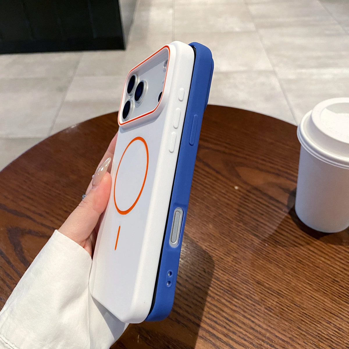 A white and blue magnetic wireless charging phone case is held above a wooden table.