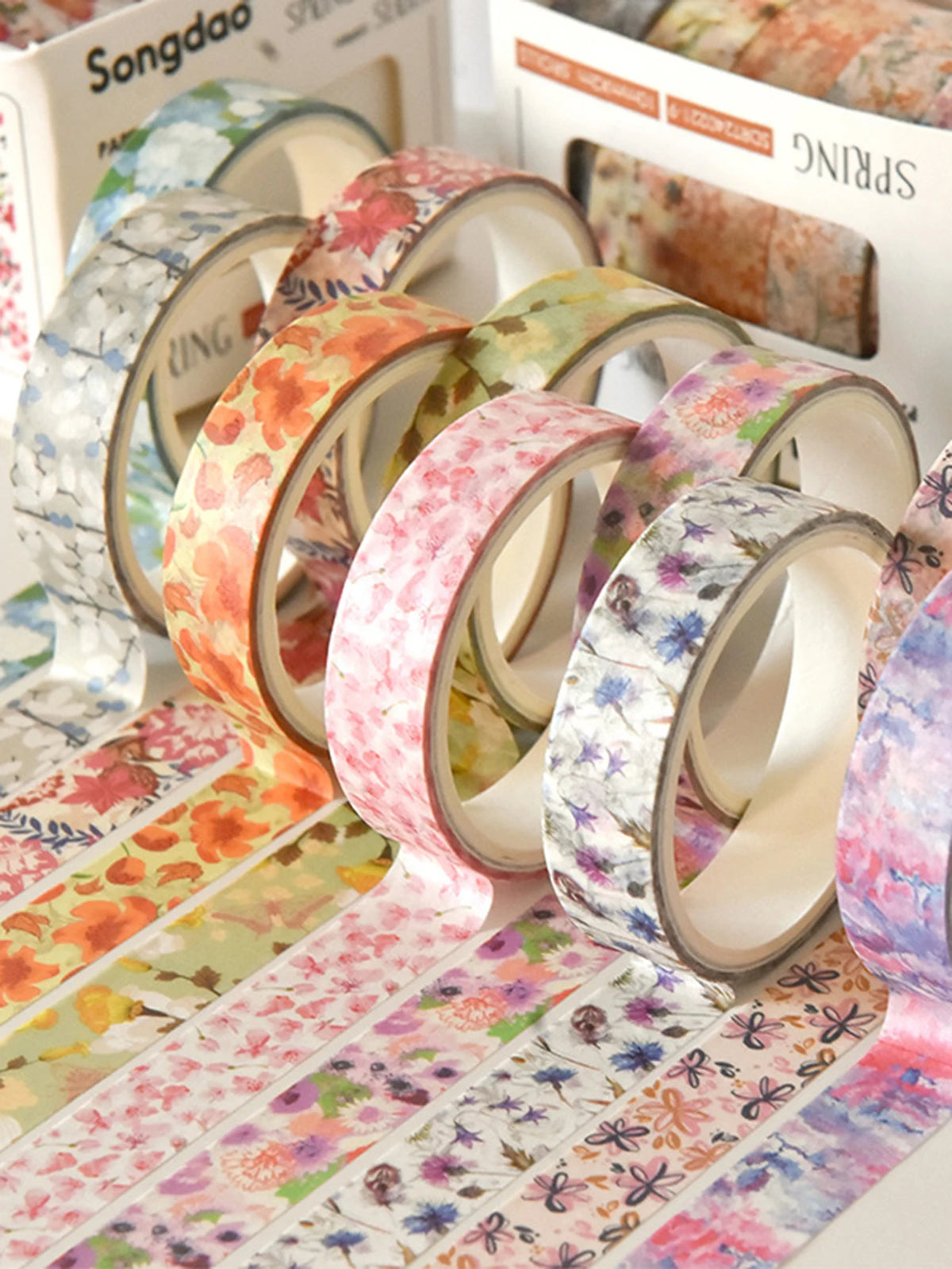 A collection of five rolls of floral washi tape in various pastel colors and patterns displayed next to a box.