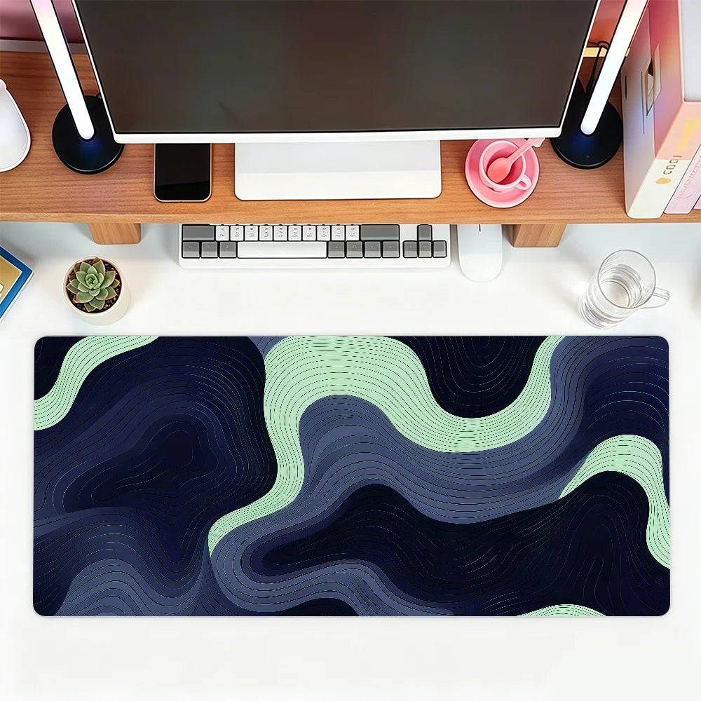 A dark blue and green abstract wave pattern mouse pad placed on a wooden desk next to a computer setup.