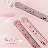 A pink plastic measuring tool shaped like a cat paw, used as a straight ruler for design or crafting.