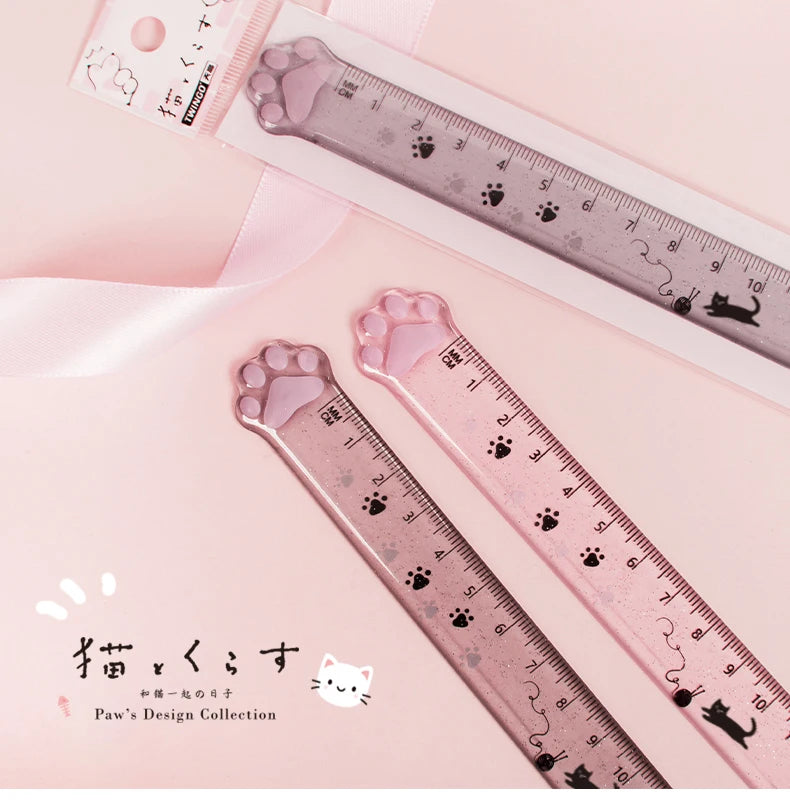 A pink plastic measuring tool shaped like a cat paw, used as a straight ruler for design or crafting.