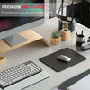 A black mouse pad with stitched edges is shown on a desk next to a laptop and other office supplies.