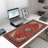 A vintage Persian rug is displayed on a white desk next to a laptop and a gaming mouse pad.