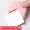 A hand is pressing a pink corner filter onto a white cardstock piece to cut the corner.