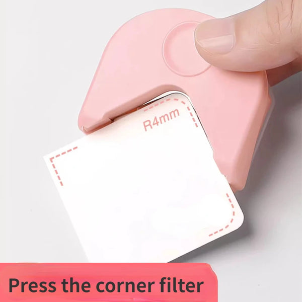 Eine Hand drückt einen rosa Eckfilter auf ein weißes Kartonstück, um die Ecke zu schneiden.