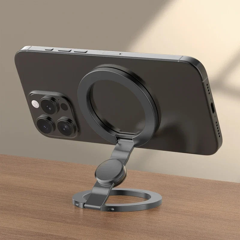 A dark gray foldable dual-sided phone stand with MagSafe compatibility shown on a wooden surface.