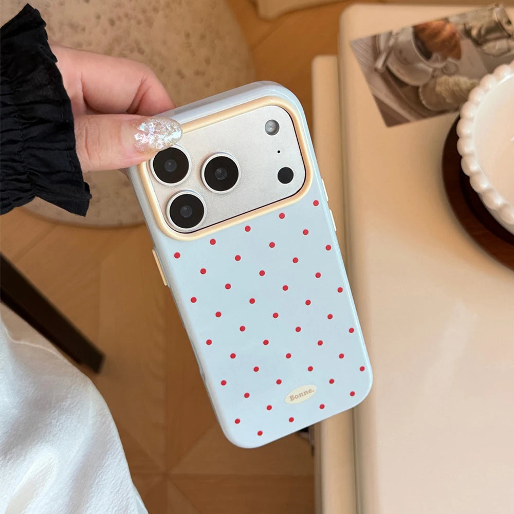 A hand holds a light blue phone case with red polka dots and gold accents against a white background.