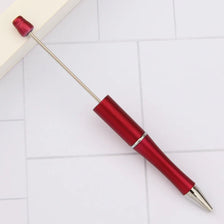 A red DIY beadable pen with a silver tip is shown resting on a white surface.