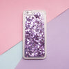 A clear phone case filled with purple glitter and holographic stars resting on a purple background.