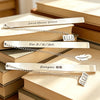 A collection of stainless steel bookmarks with engraved names and dates resting on stacked books.