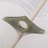 A translucent green resin thumb book stand with a cutout for holding a finger, resting on a white page.
